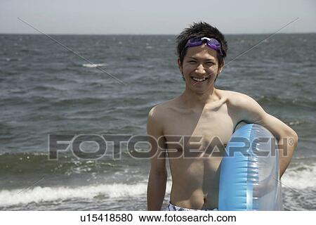 Stock Image - Portrait of a young man on beach with a lifebuoy. Fotosearch