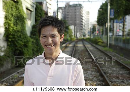 Stock Photo - Portrait of a young man smiling on railway track. Fotosearch