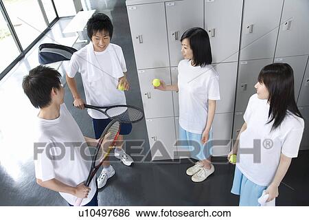 Stock Photograph - Four teenagers in gym clothes holding tennis ball and rackets in locker room. Fotosearch