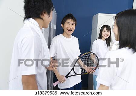 Stock Photography - Four teenagers in gym clothes smiling and talking in locker room, boy holding tennis racket. Fotosearch