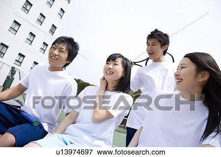 Four teenagers sitting on bench in tennis court, holding rackets View Large Photo Image Stock Photo - Four teenagers sitting on bench in tennis court, holding rackets. Fotosearch
