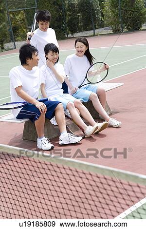 Stock Photo - Four teenagers sitting on bench in tennis court, holding rackets. Fotosearch