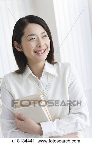 Stock Image - Girl holding textbooks, smiling, front view. Fotosearch