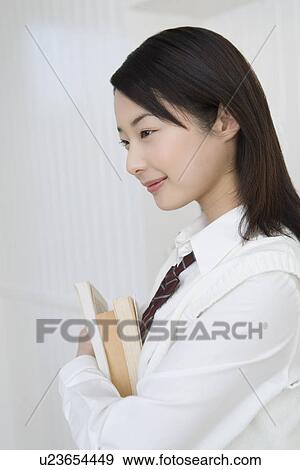 Stock Photo - Girl holding textbooks, smiling, side view. Fotosearch
