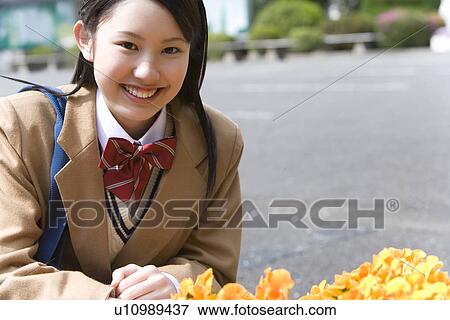 Stock Photo - High School Girl Sitting on Ground, Orange Flowers in Front of Her. Fotosearch