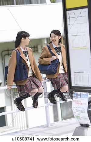 Stock Image - High School Girls Sitting on Guard Rail near Bus Stop. Fotosearch