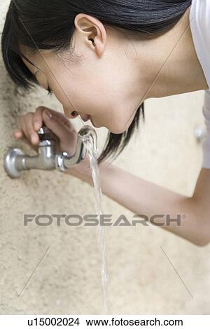 Picture - Teenage girl in gym cloth drinking water from tap. Fotosearch