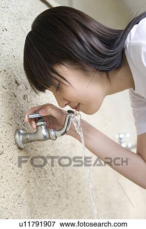 Stock Photo - Teenage girl in gym cloth drinking water from tap. Fotosearch
