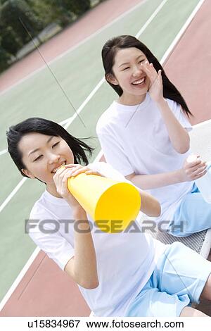 Stock Photo - Teenage girls in gym clothes cheering on bench, one holding a megaphone. Fotosearch