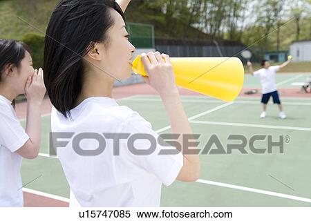 Stock Photography - Teenage girls in gym clothes cheering boys playing tennis, one holding a megaphone. Fotosearch