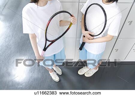 Stock Image - Teenage girls in gym clothes holding tennis rackets in locker room. Fotosearch