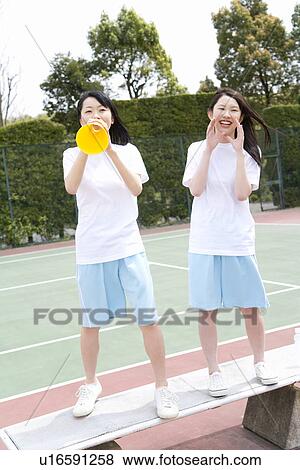 Stock Photo - Teenage girls in gym clothes standing on bench and cheering, one holding a megaphone. Fotosearch