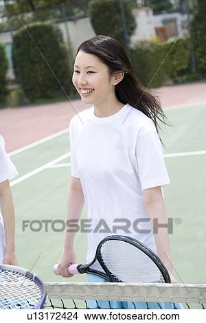 Picture - Teenage girls in tennis court, smiling and holding tennis racket. Fotosearch