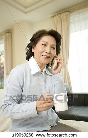 A Senior Adult Woman Holding a Cup and Talking on a Mobile Phone, Side View, Front View, Differential Focus View Large Photo Image Stock Photo - A Senior Adult Woman Holding a Cup and Talking on a Mobile Phone, Side View, Front View, Differential Focus. Fotosearch