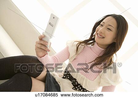 Stock Photography - A woman sitting and using a mobile phone, front view. Fotosearch