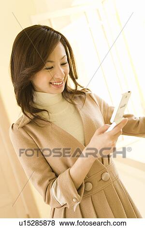 Stock Photo - A woman smiling and checking her mobile phone, front view. Fotosearch