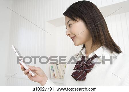 Stock Image - Girl holding and looking at mobile phone, side view. Fotosearch