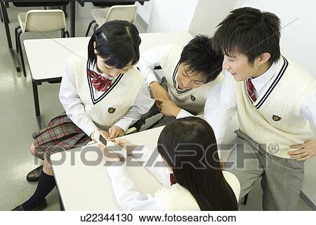 High school students sitting at desk and looking at mobile phone in classroom View Large Photo Image Stock Image - High school students sitting at desk and looking at mobile phone in classroom. Fotosearch