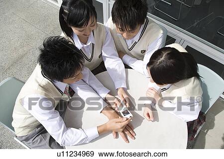 Stock Photo - High school students sitting at table and looking at mobile phone. Fotosearch