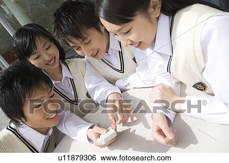 Stock Photograph - High school students sitting at table and looking at mobile phone. Fotosearch