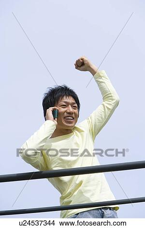 Man punching air and using mobile phone under the blue sky, front view, blue background, Japan View Large Photo Image Picture - Man punching air and using mobile phone under the blue sky, front view, blue background, Japan. Fotosearch