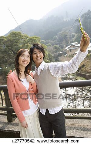 Stock Image - Man taking a picture of themselves with a mobile phone, side view, Japan. Fotosearch