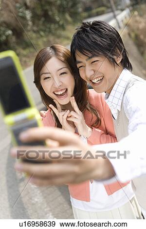 Stock Photo - Man taking a picture of themselves with a mobile phone, front view, Japan. Fotosearch