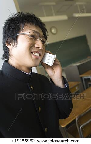 Stock Image - Teenage boy using mobile phone in classroom, smiling. Fotosearch