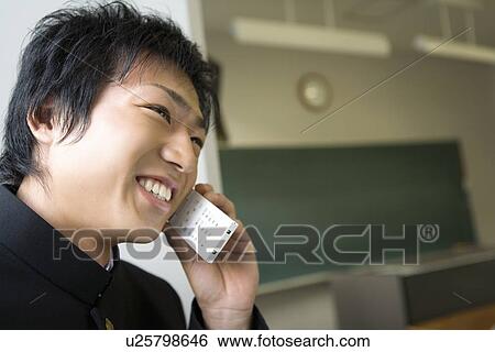 Stock Photograph - Teenage boy using mobile phone in classroom, smiling. Fotosearch