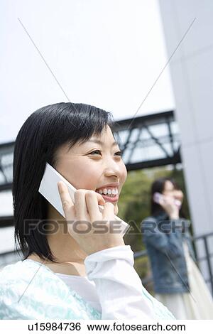 Stock Photograph - Two women using mobile phone, side view, Japan. Fotosearch