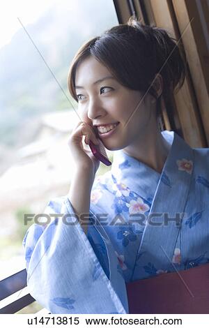 Stock Photography - Woman in Yukata using mobile phone at the window, front view, Japan. Fotosearch