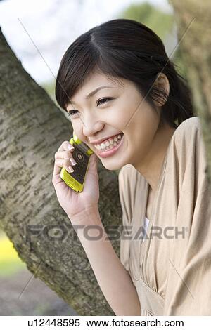 Woman leaning on a tree trunk and using a mobile phone, side view, Japan View Large Photo Image Stock Photography - Woman leaning on a tree trunk and using a mobile phone, side view, Japan. Fotosearch