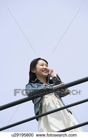 Woman leaning on the railing and using mobile phone under the blue sky, low angle view, blue background, copy space, Japan View Large Photo Image Stock Image - Woman leaning on the railing and using mobile phone under the blue sky, low angle view, blue background, copy space, Japan. Fotosearch