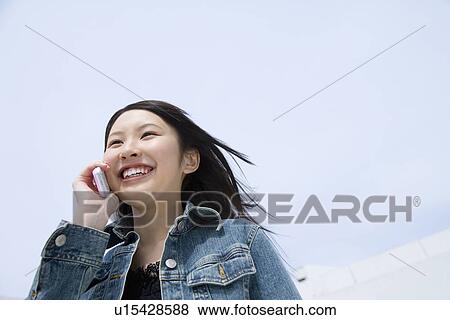 Stock Photo - Woman using mobile phone under the blue sky, low angle view, blue background, Japan. Fotosearch