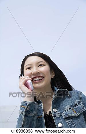 Stock Photo - Woman using mobile phone under the blue sky, low angle view, blue background, copy space, Japan. Fotosearch