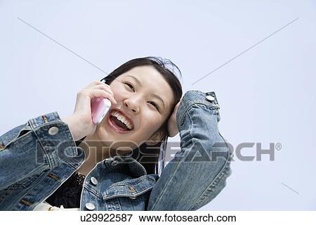 Stock Photo - Woman using mobile phone under the blue sky, low angle view, blue background, Japan. Fotosearch