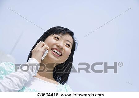 Woman using mobile phone under the blue sky, low angle view, blue background, Japan View Large Photo Image Stock Photograph - Woman using mobile phone under the blue sky, low angle view, blue background, Japan. Fotosearch