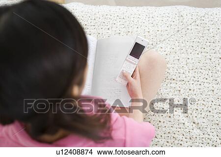Picture - Young Woman Using a Mobile Phone, Reading a Book, High Angle View. Fotosearch
