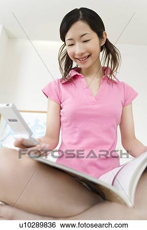 Young Woman Using a Mobile Phone, Reading a Book, Low Angle View View Large Photo Image Stock Photograph - Young Woman Using a Mobile Phone, Reading a Book, Low Angle View. Fotosearch