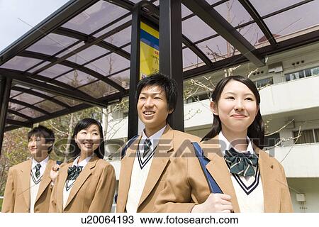 Stock Image - Four high school students standing at bus stop, smiling. Fotosearch