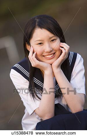 Stock Photo - Portrait of a teenage girl sitting and resting chin in hands in schoolyard, smiling and looking at camera. Fotosearch