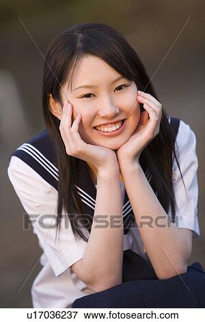 Stock Photo - Portrait of a teenage girl sitting and resting chin in hands in schoolyard, smiling and looking at camera. Fotosearch