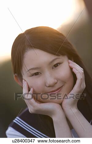 Portrait of a teenage girl sitting and resting chin in hands in schoolyard, smiling and looking at camera View Large Photo Image Stock Photo - Portrait of a teenage girl sitting and resting chin in hands in schoolyard, smiling and looking at camera. Fotosearch
