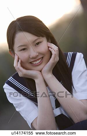 Stock Photography - Portrait of a teenage girl sitting and resting chin in hands in schoolyard, smiling and looking at camera. Fotosearch