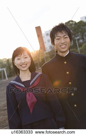 Stock Image - Portrait of teenage couple standing in schoolyard, smiling and looking at camera. Fotosearch