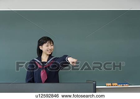 Teenage girl standing in front of blackboard and pointing forward, smiling, green background View Large Photo Image Stock Photograph - Teenage girl standing in front of blackboard and pointing forward, smiling, green background. Fotosearch
