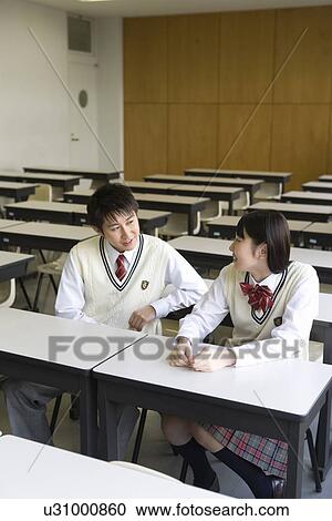 Stock Image - High school students sitting at desk and talking in classroom. Fotosearch