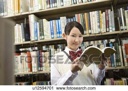 Portrait of a teenage girl holding a book in front of bookcase, smiling and looking at camera View Large Photo Image Stock Image - Portrait of a teenage girl holding a book in front of bookcase, smiling and looking at camera. Fotosearch