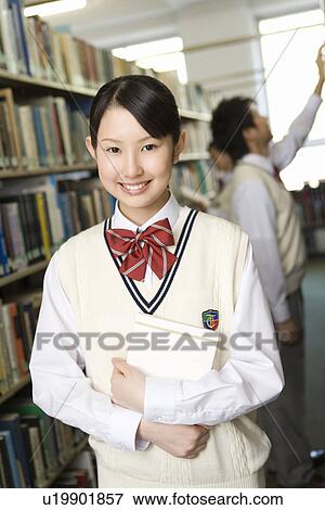 Stock Photo - Portrait of a teenage girl holding a book in library, smiling and looking at camera. Fotosearch