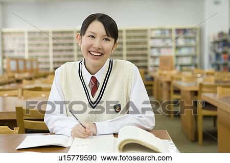 Stock Image - Portrait of a teenage girl studying in library, smiling. Fotosearch